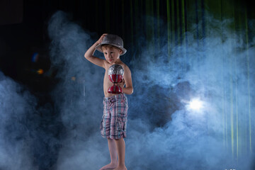A little boy circus performer performs against the backdrop of stage lighting.