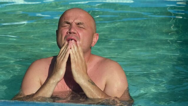 Man aching from extreme heat on sweltering summer day escapes high temperature in a cool water of swimming pool. Person is overheated and washes up in pool outside