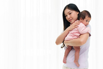 mother holding newborn baby burping after feeding milk on window background