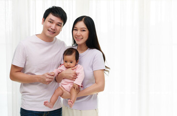 cheerful father and mother holding newborn baby on window background. happy family concept