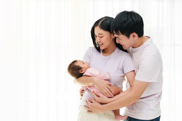 cheerful father and mother holding and hugging with newborn baby on window background. happy family concept