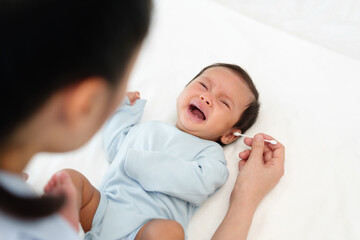 mother using cotton bud to cleaning ear of crying newborn baby on bed