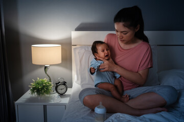 mother holding burping and crying baby after feeding milk on bed at night