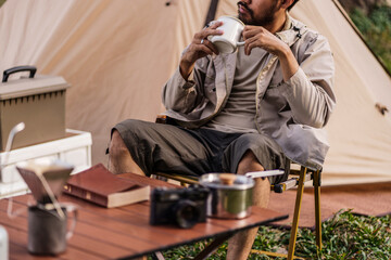 Asian man drinking coffee enjoying camping outdoors in nature. Man traveler hands holding cup of coffee.