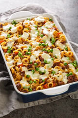 Anelli pasta casserole with tomatoes, cheese, minced meat, green peas, carrots and celery close-up in a baking dish on the table. Vertical