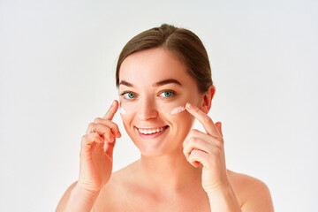 Fototapeta premium Portrait of young woman applying facial cream for beautiful healthy skin on white background
