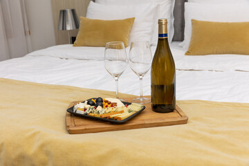 Antipasto appetizer cheese board wine and glases on a hotel bed - obrazy, fototapety, plakaty