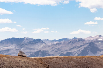 Off-road vehicle moving on dirt road by mountain against sky