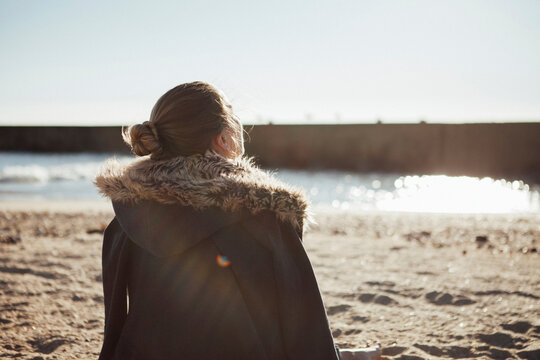 Rear view of woman sitting on sand against clear sky at beach