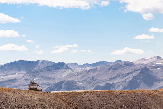 Off-road vehicle moving on dirt road by mountain against sky