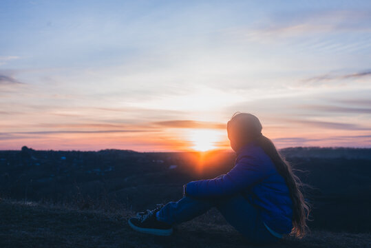 A young girl on the background of the sunset. Evening in nature in the mountains. Prayer against the background of the sky.