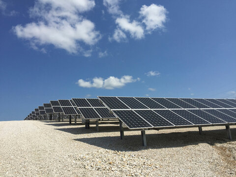 Solar panels on field against blue sky during sunny day