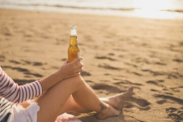 Low section of woman holding beer bottle while relaxing at beach