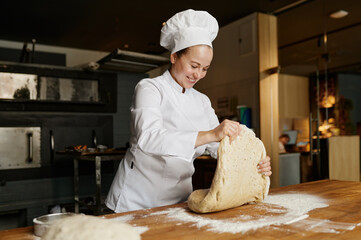 Female baker kneading or forming dough while working at bakehouse