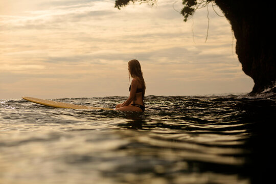 Woman surfing in sea against cloudy sky during sunset