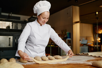 Young woman baker working in bakery, forming baguettes from raw dough