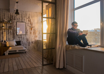 Man using tablet computer while sitting on window sill at home