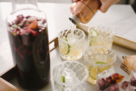 Cropped hand of man pouring drinks in glasses on table at home