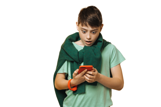 Shocked boy dressed in a green t-shirt and sweater tied up over his neck, holds phone, looks screen with wide open eyes, amazed by received message, over transparent background. Education concept.