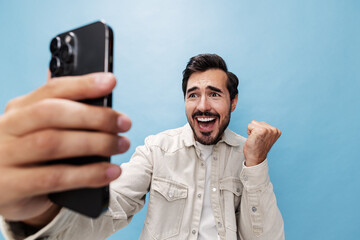 Portrait of a man brunette smile looking at the phone blogger with a beard taking selfies, on a blue background in a white T-shirt and jeans, copy space