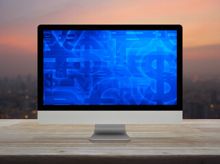 Financial currency symbol on desktop computer monitor screen on wooden table over blur of cityscape on warm light sundown