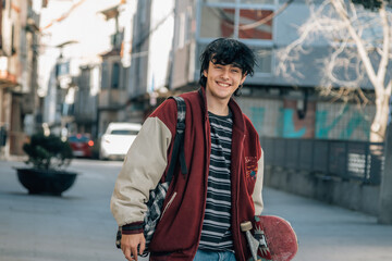 smiling teenager in the city carrying backpack and skateboard