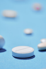 Medicine and drug concept. Close up shot of white pill on blue background with different tablets on it out of focus.