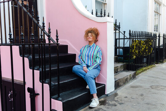 Young woman with Afro hair sits on doorstep, clearing her mind.