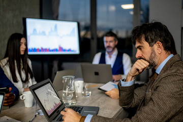 Financial broker analyzes data in the office with colleagues, working late at night