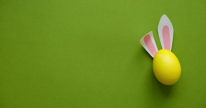 Easter rabbit ears on a yellow egg on a green background with a place for text. Looped 4K stop motion animation