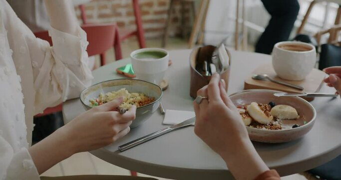 Close-up of female hands with forks eating delicious food in cafe while women enjoying lunch together. Meal and modern lifestyle concept.