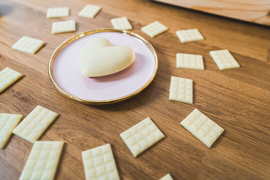 Valentine's Day Concept. Sweet white chocolate heart on pink plate surrounded by small white chocolate bars. Wooden table. High quality photo