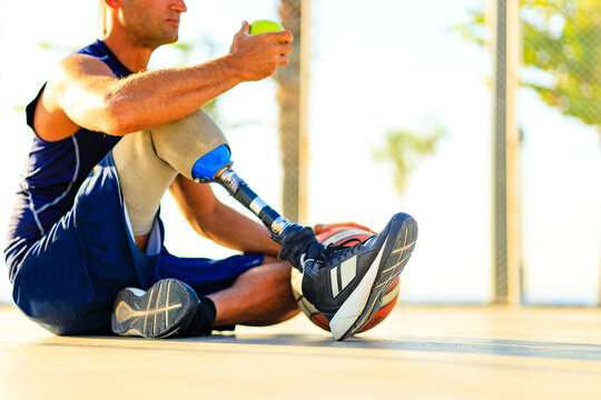 man with leg prosthesis playing basketball in tropical sea side at sumset time eating an apple