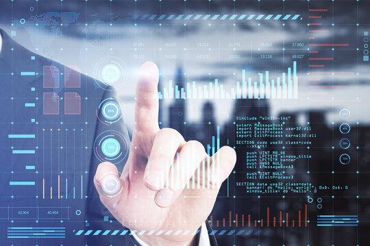 Close up of businessman hand pointing at glowing digital interface with business charts and coding on blurry city background. Future and cyberspace concept. Double exposure.
