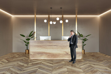 Front view on pensive businessman near stylish reception desk made from natural wooden slab with...