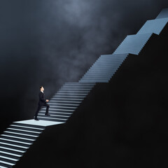 Long career and long way to success concept with businessman climbs dark stairs illuminated from above on abstract dark foggy background