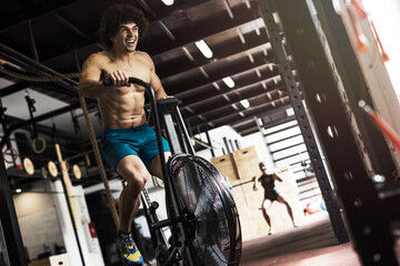 Fototapeta na wymiar Young man using air bike for cardio workout at sports center.