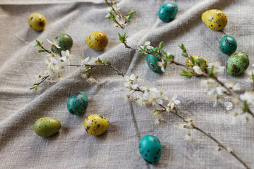 Stylish easter eggs and blooming cherry flowers on rustic table. Happy Easter! Rustic easter still life. Natural painted quail eggs and cherry blossoms on linen fabric