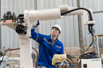Male engineer worker wear safety uniform, helmet and gloves control robot arm welding at production line plant factory