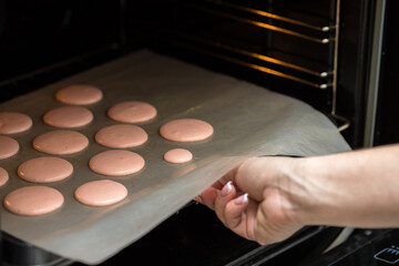 a woman confectioner puts macarons cookies in the oven for baking. hands close up. home bakery concept.