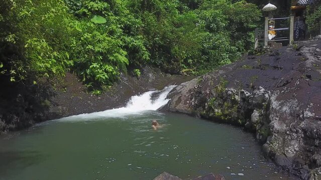 Beautiful blonde woman swims in waterfall pool in Indonesian jungle