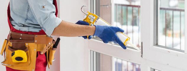 Construction worker sealing window with caulk indoors