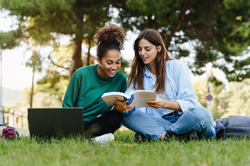 University friends studying together at university campus - Female girl students sitting on grass reading book 