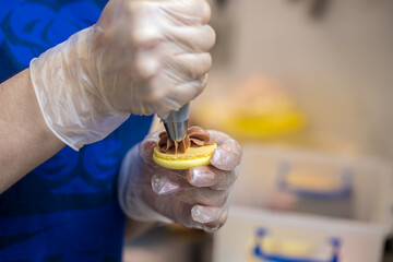 the pastry chef squeezes the filling onto macarons cookies. close-up. home bakery concept.