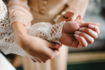 The bridesmaid fastens the buttons on the sleeve of the bride's dress. The bride straightens her...