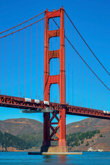 Majestic golden gate bridge with suspension wires and red girders on exterior near blue clear sky and ocean mountains