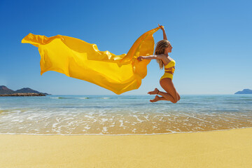 Happy young woman with a yellow light one Cloth jumping at sand beach. Relaxing, fun, and enjoy holiday at tropical paradise beach with blue sky. Girl in summer vacation. - Powered by Adobe