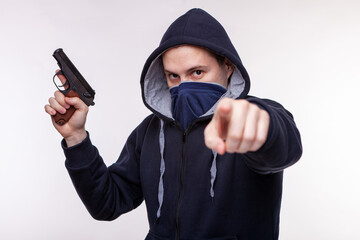 A robber with a gun points his finger at the victim. A man with a gun. Aggressive man in a mask and...
