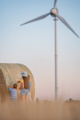 Children with a coil of hay on the background of a wind turbine. Little girl and boys in front of...