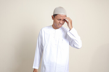 Portrait of attractive Asian muslim man in white shirt having a migraine, touching his temple. Headache disease concept. Isolated image on gray background